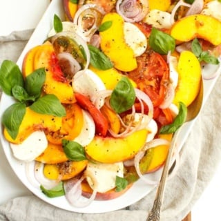 peach caprese salad with heirloom tomatoes and fresh mozzarella on a white platter